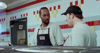 Movie still from “Funny People” (2009), directed by Judd Apatow – Two men standing in front of a counter talking to each other; Close Up shot, Over the shoulder angle