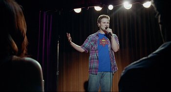 Movie still from “Funny People” (2009), directed by Judd Apatow – A man standing on a stage holding a microphone; Medium shot, Over the shoulder angle