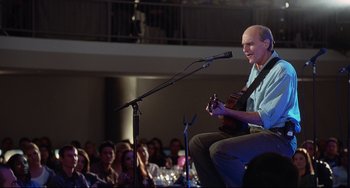 Movie still from “Funny People” (2009), directed by Judd Apatow – A man sitting in front of a microphone on a stage; Medium shot, Over the shoulder angle