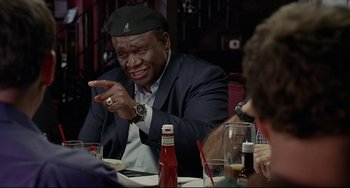 Movie still from “Funny People” (2009), directed by Judd Apatow – A man sitting at a table in front of a group of people; Close Up shot, Over the shoulder angle