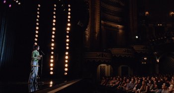 Movie still from “Funny People” (2009), directed by Judd Apatow – A group of people sitting in front of a microphone; Extreme Wide shot, High angle