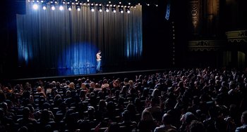 Movie still from “Funny People” (2009), directed by Judd Apatow – An audience watching a man stand up on a stage; Extreme Wide shot, High angle
