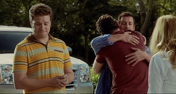 Movie still from “Funny People” (2009), directed by Judd Apatow – A group of people hug in front of a car; Medium shot, Over the shoulder angle