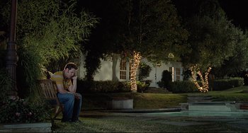 Movie still from “Funny People” (2009), directed by Judd Apatow – A man sitting on a chair in the grass at night; Wide shot, High angle