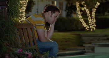 Movie still from “Funny People” (2009), directed by Judd Apatow – A man sitting on top of a wooden bench next to flowers; Medium shot, High angle