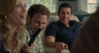 Movie still from “Funny People” (2009), directed by Judd Apatow – Two men and a woman sitting on a couch laughing; Medium shot, Over the shoulder angle