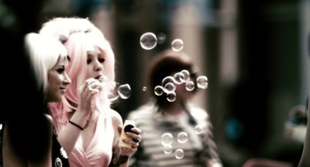 Movie still from “Gamer” (2009), directed by Mark Neveldine – A woman blowing soap bubbles in front of another woman; Medium shot, Low angle