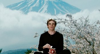 Movie still from “Gamer” (2009), directed by Mark Neveldine – A man sitting in front of a mountain holding a cup; Medium shot, Low angle