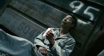 Movie still from “Gamer” (2009), directed by Mark Neveldine – A man sitting on the ground holding a piece of food; Medium shot, Overhead angle