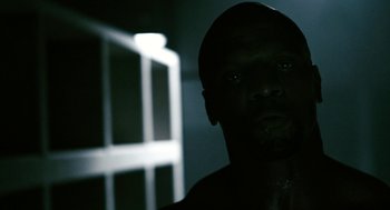 Movie still from “Gamer” (2009), directed by Mark Neveldine – A man with a dark face is in a dark room; Close Up shot, Low angle