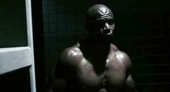 Movie still from “Gamer” (2009), directed by Mark Neveldine – A black man with a shaved head is posing for the camera; Medium shot, Low angle