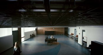 Movie still from “Gamer” (2009), directed by Mark Neveldine – A man sitting at a table in a large room; Extreme Wide shot, High angle
