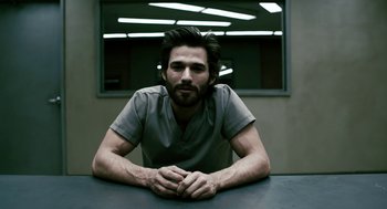 Movie still from “Gamer” (2009), directed by Mark Neveldine – A man sitting at a table with his arms crossed; Medium shot, Low angle