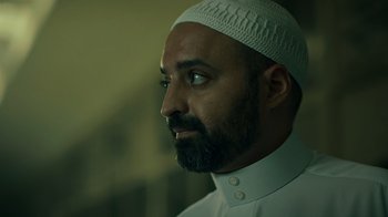 Movie still from “Ganglands” (2021), created by Julien Leclercq – A person with a beard wearing a hat; Close Up shot, Low angle