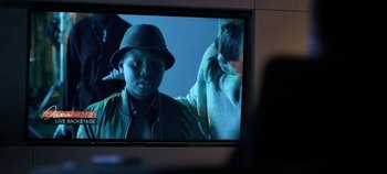 Movie still from “Black Mirror” (2011), created by Charlie Brooker – A man wearing a hat is on a television screen; Close Up shot, Over the shoulder angle