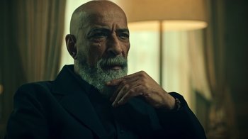 Movie still from “Ganglands” (2021), created by Julien Leclercq – An older man with a beard and a watch; Close Up shot, Low angle