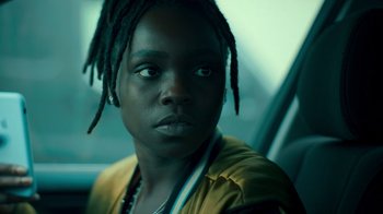 Movie still from “Ganglands” (2021), created by Julien Leclercq – A woman with dreads sitting in a car looking at the camera; Close Up shot, High angle