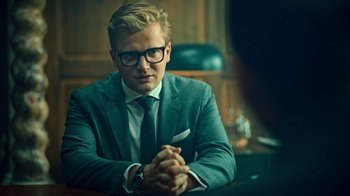 Movie still from “Ganglands” (2021), created by Julien Leclercq – A man sitting at a table with his hands crossed; Close Up shot, Over the shoulder angle