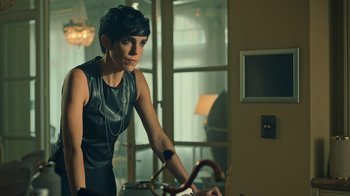 Movie still from “Ganglands” (2021), created by Julien Leclercq – A woman leaning on a table in a living room; Medium shot, Over the shoulder angle