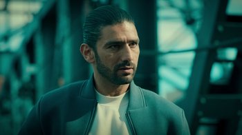 Movie still from “Ganglands” (2021), created by Julien Leclercq – A person wearing a jacket; Close Up shot, Over the shoulder angle