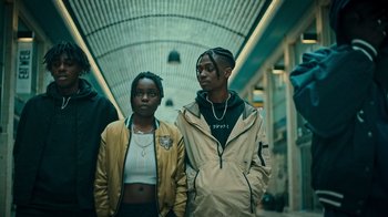 Movie still from “Ganglands” (2021), created by Julien Leclercq – A couple of people standing next to each other in a building; Medium shot, Low angle