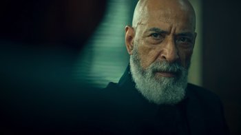 Movie still from “Ganglands” (2021), created by Julien Leclercq – An old man with a beard and a white mustache; Close Up shot, Over the shoulder angle