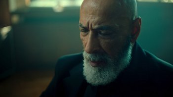 Movie still from “Ganglands” (2021), created by Julien Leclercq – An old man with a beard and a black suit; Close Up shot, Low angle
