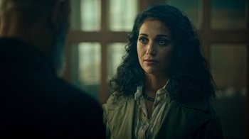 Movie still from “Ganglands” (2021), created by Julien Leclercq – A woman with long curly black hair standing next to a man; Close Up shot, Over the shoulder angle