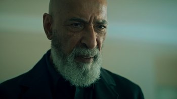 Movie still from “Ganglands” (2021), created by Julien Leclercq – An older man with a beard and a black suit; Close Up shot, Low angle