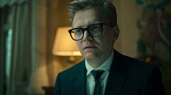 Movie still from “Ganglands” (2021), created by Julien Leclercq – A man in a suit and tie wearing glasses; Close Up shot, Low angle