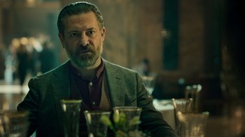Movie still from “Ganglands” (2021), created by Julien Leclercq – A man sitting at a dinner table looking at the camera; Close Up shot, Low angle