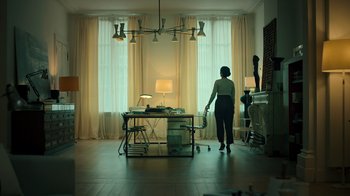 Movie still from “Ganglands” (2021), created by Julien Leclercq – A woman standing in front of a desk in front of a window; Wide shot, Low angle