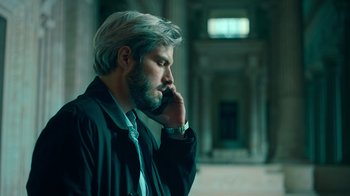 Movie still from “Ganglands” (2021), created by Julien Leclercq – A man with a beard talking on a cell phone; Medium shot, Low angle