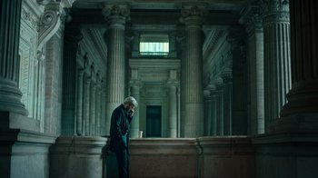Movie still from “Ganglands” (2021), created by Julien Leclercq – An older man is standing in a building with a cup; Wide shot, Low angle