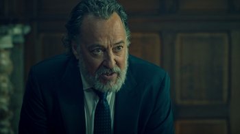 Movie still from “Ganglands” (2021), created by Julien Leclercq – An older man in a suit and a tie; Close Up shot, Over the shoulder angle