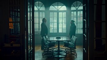 Movie still from “Ganglands” (2021), created by Julien Leclercq – Two men standing around a round table in a room; Wide shot, High angle