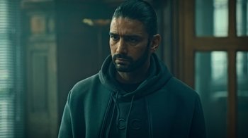 Movie still from “Ganglands” (2021), created by Julien Leclercq – A person wearing a hooded sweatshirt; Close Up shot, Over the shoulder angle