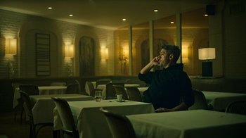 Movie still from “Ganglands” (2021), created by Julien Leclercq – A man sitting at a table in front of a glass of water; Wide shot, Low angle