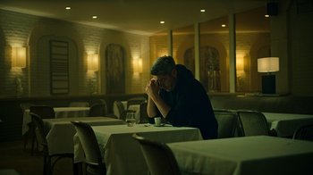 Movie still from “Ganglands” (2021), created by Julien Leclercq – A man sitting at a table with his head on his hands; Medium shot, Low angle
