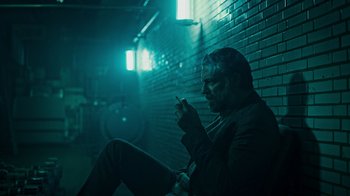 Movie still from “Ganglands” (2021), created by Julien Leclercq – A man sitting on the ground in a dark room; Medium shot, Low angle