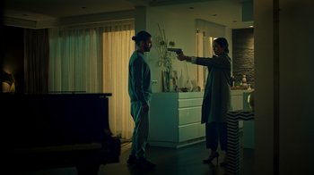 Movie still from “Ganglands” (2021), created by Julien Leclercq – A man and a woman are standing in a living room; Wide shot, Over the shoulder angle