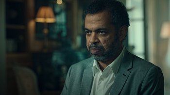 Movie still from “Ganglands” (2021), created by Julien Leclercq – A person wearing a suit and tie; Close Up shot, Over the shoulder angle