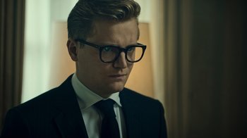 Movie still from “Ganglands” (2021), created by Julien Leclercq – A man in a suit and tie wearing glasses; Close Up shot, Low angle