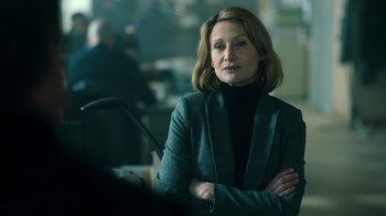 Movie still from “Ganglands” (2021), created by Julien Leclercq – A woman with her arms crossed standing in a room; Close Up shot, Over the shoulder angle