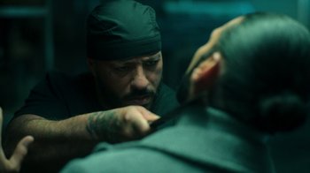 Movie still from “Ganglands” (2021), created by Julien Leclercq – A man with a beard cutting another man's hair; Close Up shot, Over the shoulder angle