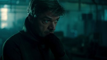 Movie still from “Ganglands” (2021), created by Julien Leclercq – A person with his hand under his chin; Close Up shot, Low angle