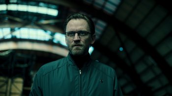 Movie still from “Ganglands” (2021), created by Julien Leclercq – A person wearing glasses and a jacket; Close Up shot, Low angle