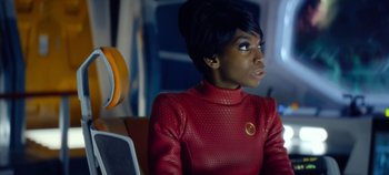 Movie still from “Black Mirror” (2011), created by Charlie Brooker – A woman in a red outfit sitting in a chair; Close Up shot, Over the shoulder angle