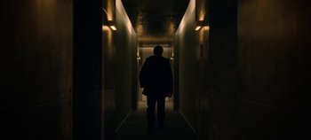 Movie still from “Black Mirror” (2011), created by Charlie Brooker – A man is walking down a dark hallway at night; Wide shot, Low angle