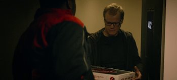 Movie still from “Black Mirror” (2011), created by Charlie Brooker – A man sitting in front of a box of pizza; Medium shot, Over the shoulder angle